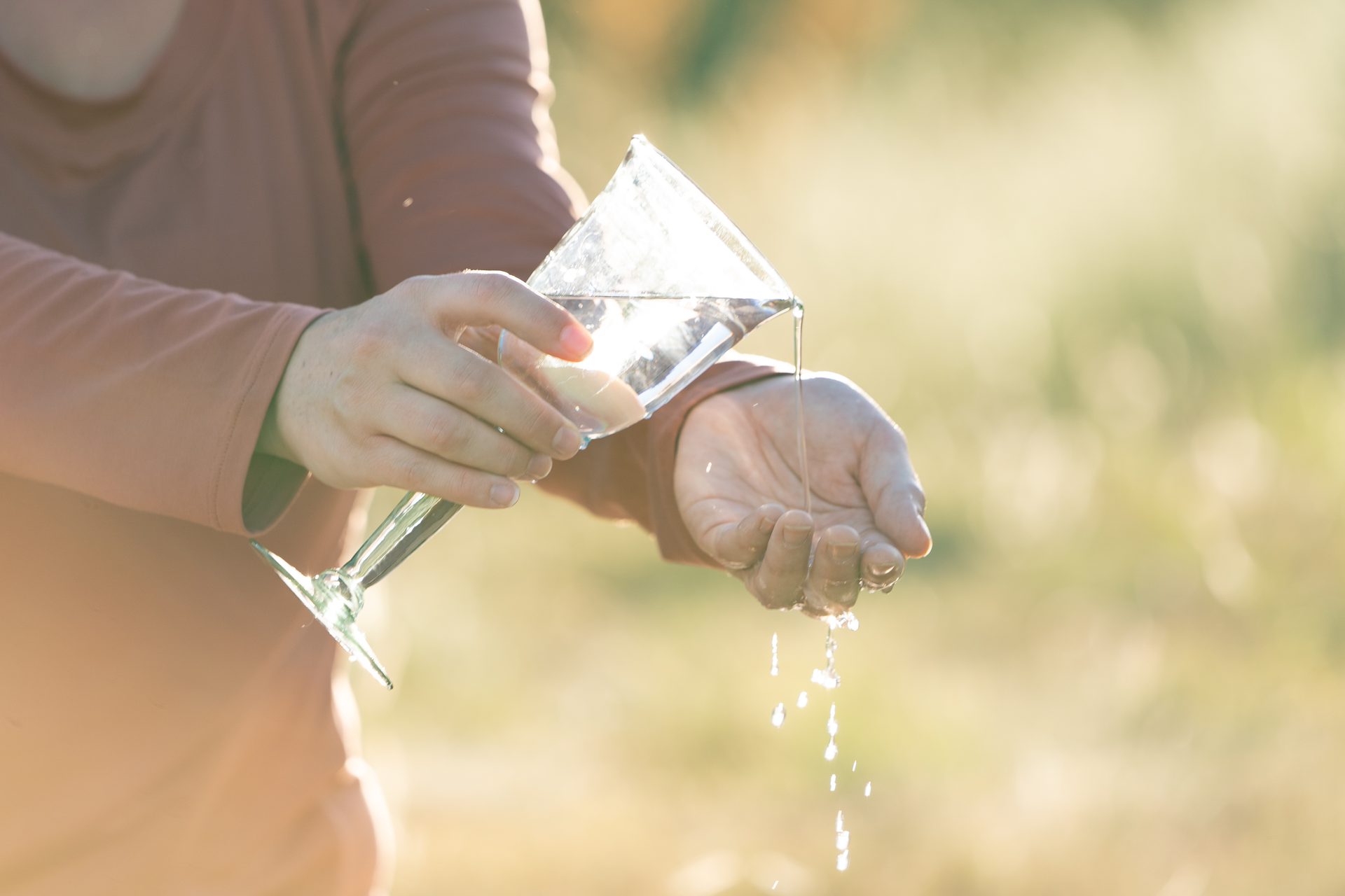 Water poured from a glass into open hands in golden light